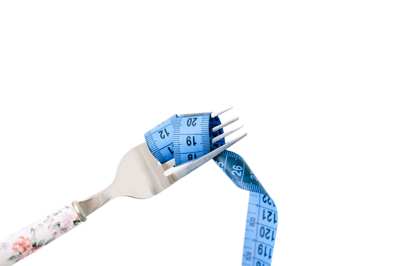 About A fork entwined with a blue measuring tape, symbolizing dieting and weight management.